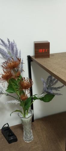 a vase with flowers on a table next to a clock at Seu Belém - Sua Estadia Paraense in Belém