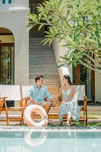 a man and woman sitting on a bench next to a swimming pool at Én Retreat Hoi An in Hoi An
