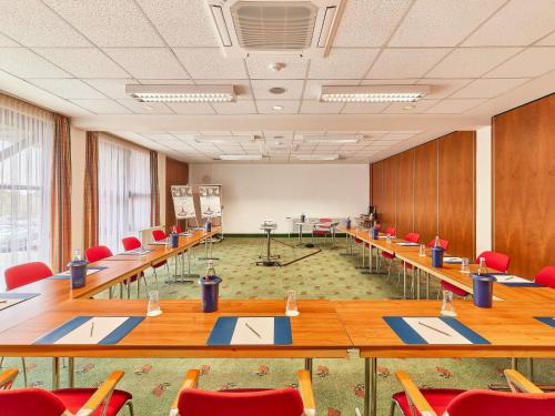 a conference room with long tables and red chairs at Mercure Hotel Bad Duerkheim An Den Salinen in Bad Dürkheim