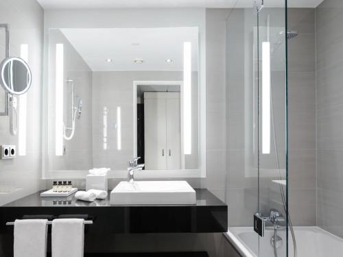 a bathroom with a sink and a mirror and a shower at Pullman Berlin Schweizerhof in Berlin