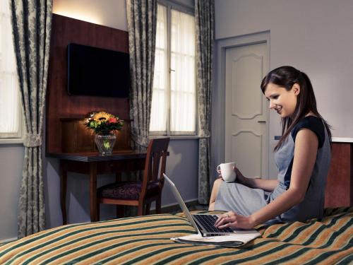 a woman sitting on a bed using a laptop computer at Mercure Grand Hotel Biedermeier Wien in Vienna