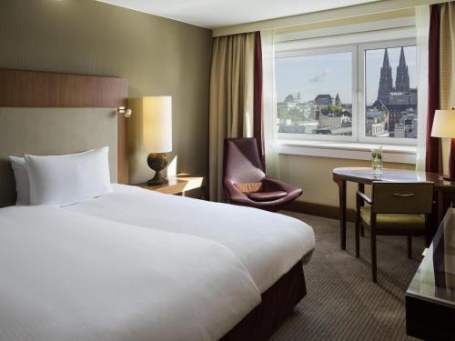 a hotel room with a bed and a desk and a window at Pullman Cologne in Cologne