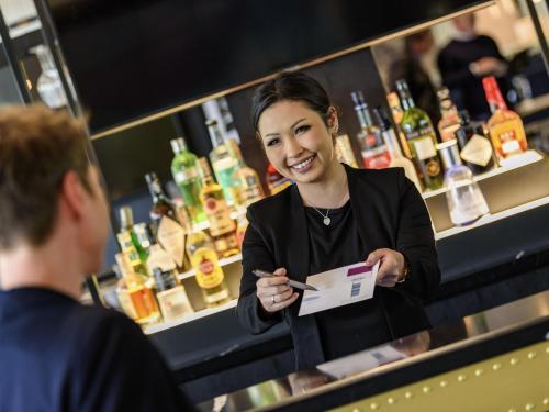 a woman standing in front of a bartender at Mercure Neu-Isenburg in Neu Isenburg