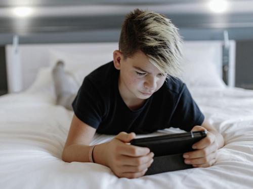 a young boy laying on a bed looking at a tablet at Novotel Hannover in Hannover