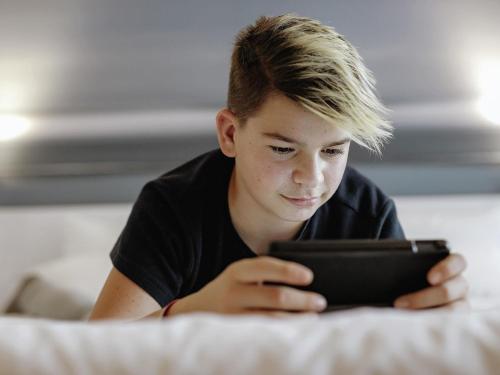 a young boy laying on a bed looking at a tablet at Novotel Hannover in Hannover