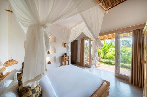 a bedroom with a white bed with a canopy at Rumah Kita Ecolodge in Ubud