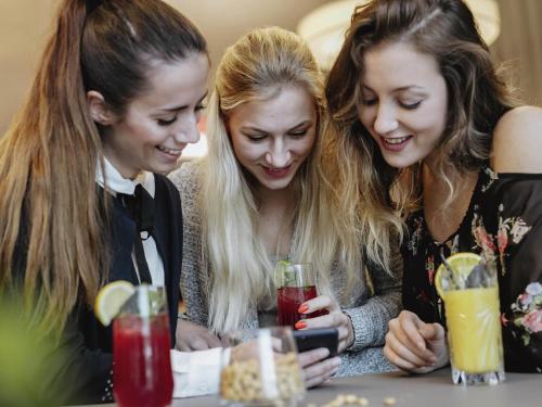 a group of three girls looking at a cell phone at Novotel Hildesheim in Hildesheim