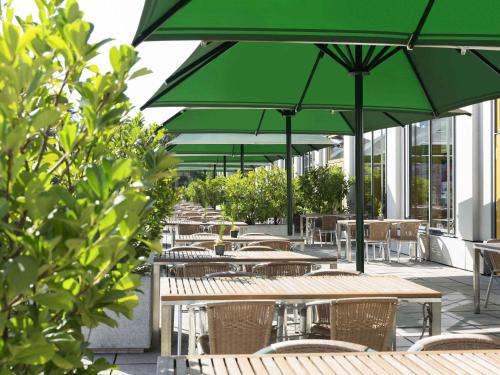 a row of tables and chairs with green umbrellas at Novotel Karlsruhe City in Karlsruhe