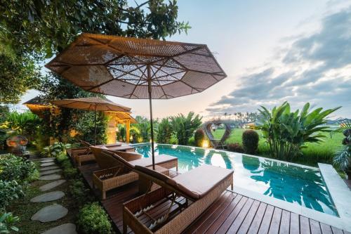 a pool with chairs and an umbrella next to a swimming pool at Rumah Kita Ecolodge in Ubud