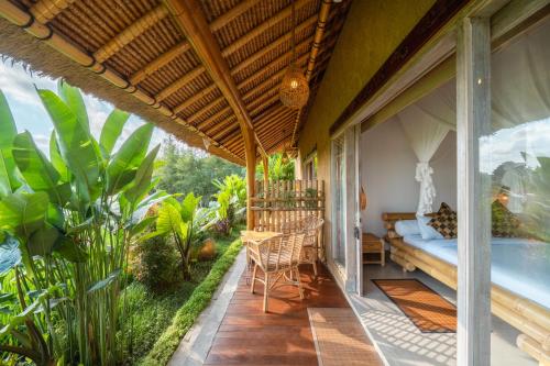 a porch with a bed and a table and chairs at Rumah Kita Ecolodge in Ubud