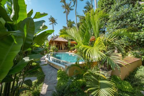 a pool in a garden with palm trees and a gazebo at Rumah Kita Ecolodge in Ubud