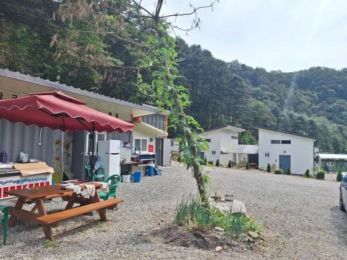 einen Picknicktisch mit einem roten Regenschirm neben einem Gebäude in der Unterkunft Chuncheon Cracra Pension in Madang-gol