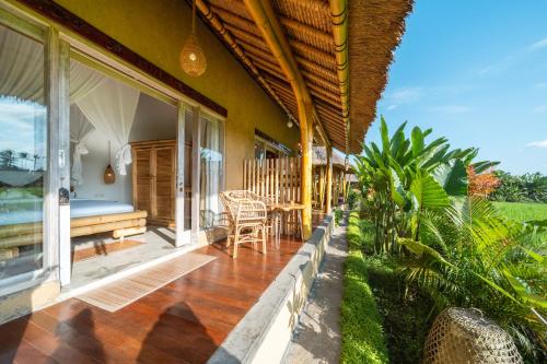 a porch of a house with a bed and a table at Rumah Kita Ecolodge in Ubud