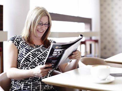 a woman sitting at a table reading a magazine at Novotel Reading Centre in Reading