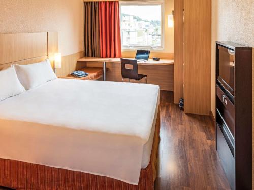 a hotel room with a bed and a desk with a laptop at ibis Blumenau in Blumenau
