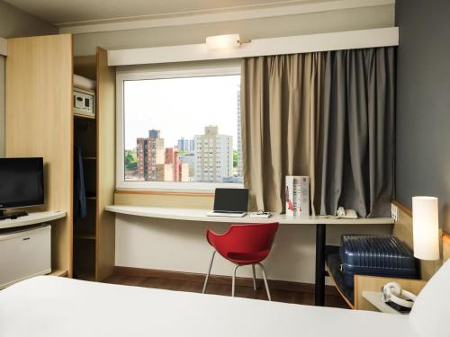 a hotel room with a desk and a window at ibis Campinas in Campinas