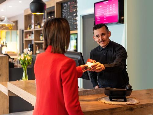 a woman standing at a barber shop with a customer at ibis Nuits Saint Georges in Nuits-Saint-Georges