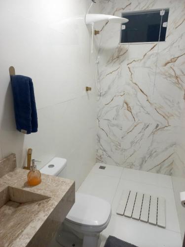 a bathroom with a white toilet and a marble wall at RECANTO dos SONHOS - MASSARANDUPIÓ - SUÍTES & QUARTOS in Massarandupio