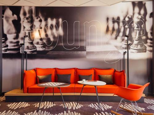 an orange couch and two tables in a room at ibis La Ciotat in La Ciotat