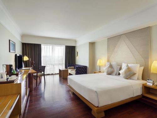 a hotel room with a large bed and a living room at Novotel Semarang in Semarang