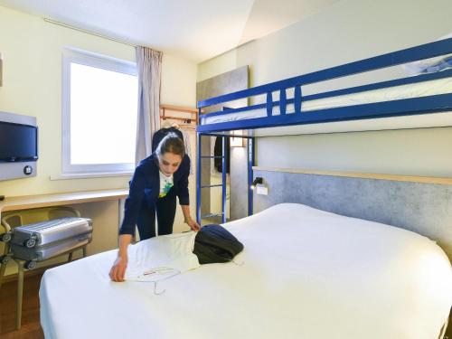 a woman is making a bed in a hospital room at ibis Budget Charleroi Airport in Charleroi