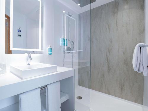 a white bathroom with a sink and a shower at Novotel Luxembourg Centre in Luxembourg