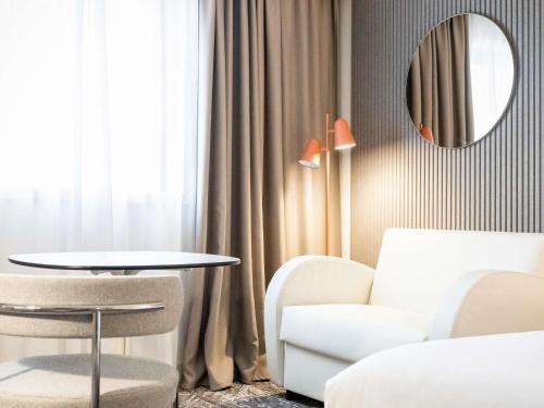 a living room with a table and a chair and a mirror at Novotel Paris 13 Porte d'Italie in Le Kremlin-Bicêtre