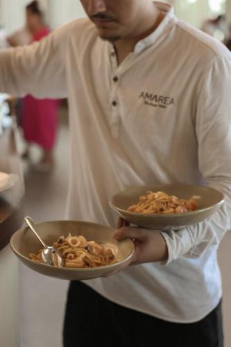 a man holding a plate of pasta in at Amarea Boutique Hotel in Dhërmi