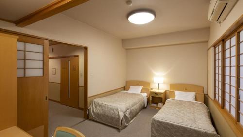 a room with two beds and a table with a lamp at Hotel Symphony Annex Sagae Onsen in Sagae