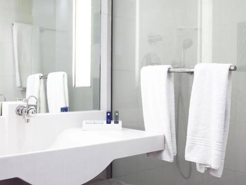 a white bathroom with a sink and a mirror at Novotel Le Havre Centre Gare in Le Havre