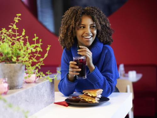 a woman sitting at a table with a sandwich and a drink at ibis Santo Andre in Santo André