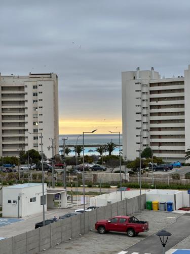 a red car parked in a parking lot near two tall buildings at Dpto con terraza vista al mar y faro in La Serena
