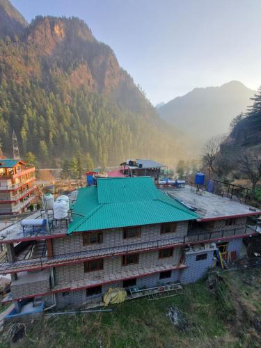 a building with a green roof next to a mountain at Shanti cafe and stay in Kasol