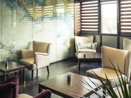 a waiting room with chairs and tables and a mural at Hotel Mercure Rennes Cesson in Cesson-Sévigné