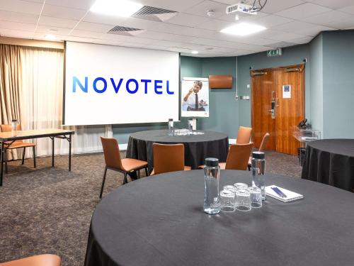 a conference room with tables and chairs and a screen with no yielded at Novotel Cardiff Centre in Cardiff