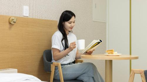 a woman sitting at a table reading a book at Centum Mark Kimstay Yangyang in Yangyang
