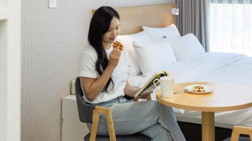 a woman sitting on a bed eating a slice of pizza at Centum Mark Kimstay Yangyang in Yangyang