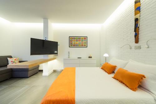 ein weißes Schlafzimmer mit einem großen Bett mit einer orangefarbenen Decke in der Unterkunft Suites Garden Loft Miro in Las Palmas de Gran Canaria