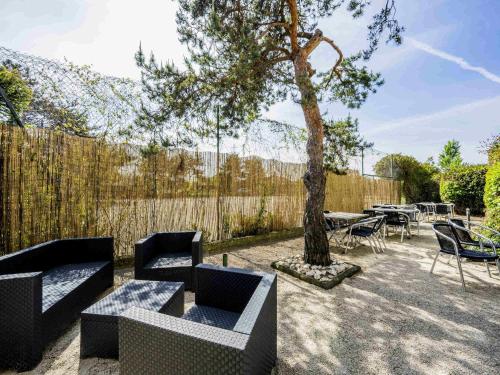 a patio with couches and a tree and a table and chairs at Mercure Vienne Sud Chanas in Chanas