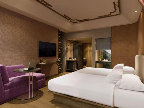 a bedroom with a large white bed and a purple chair at Mercure Surabaya Grand Mirama in Surabaya