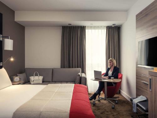 a woman sitting at a table with a laptop in a hotel room at Mercure Paris Boulogne in Boulogne-Billancourt