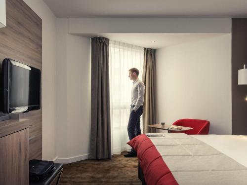 a man standing in a hotel room looking out the window at Mercure Paris Boulogne in Boulogne-Billancourt