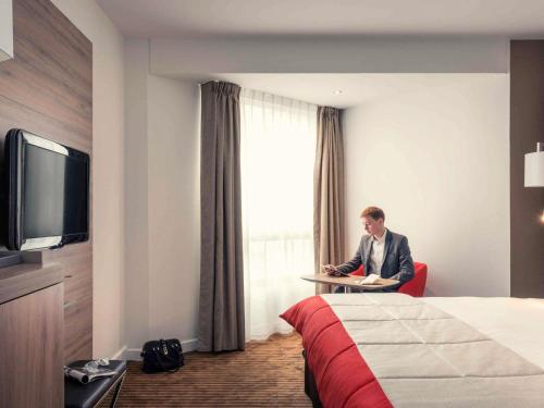 a man sitting at a table in a hotel room at Mercure Paris Boulogne in Boulogne-Billancourt