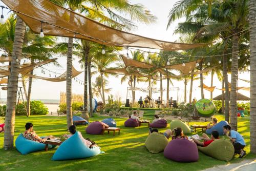 a group of people sitting on the grass under palm trees at The Cliff Resort & Residences in Mui Ne