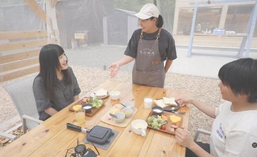 een groep mensen die rond een tafel met eten staan bij Glamp Sora Furano in Nakafurano