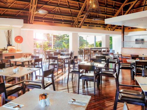 a dining room with tables and chairs and windows at Novotel Nadi in Nadi