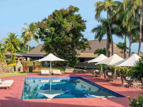 a swimming pool with tables and chairs and umbrellas at Novotel Nadi in Nadi