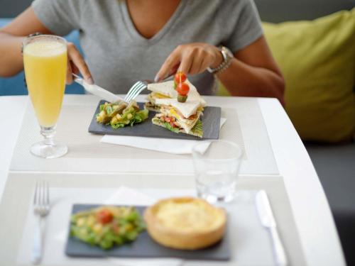a woman sitting at a table with a sandwich and a drink at Ibis Casablanca Sidi Maarouf in Casablanca
