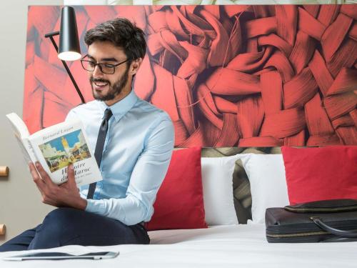 a man sitting on a bed reading a book at Ibis Casablanca Sidi Maarouf in Casablanca
