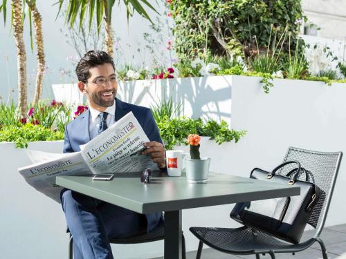 a man sitting at a table reading a newspaper at Ibis Casablanca Sidi Maarouf in Casablanca